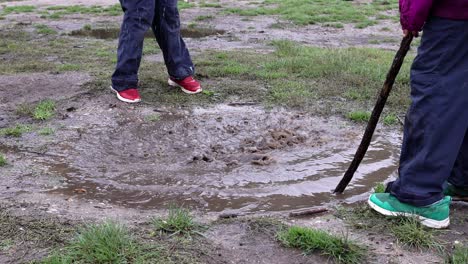 two ethnically diverse children playing with sticks in a muddy puddle