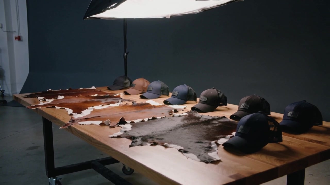 Kamera menggeser menyingkap meja di studio dengan kulit sapi dan topi baseball di bawah softbox untuk penataan.
