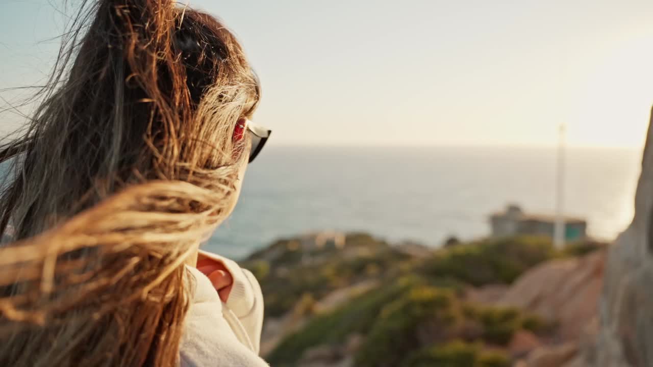 Young woman watching the sunset on the sea while the wind sways her hair with highlights