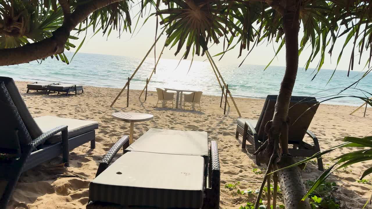 Sunlit beach with lounge chairs and palm trees, capturing a serene coastal atmosphere in Phuket, Thailand