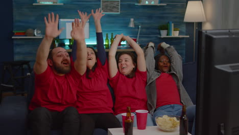 multiethnic friends sitting on couch in front of tv watching football cheering team goal