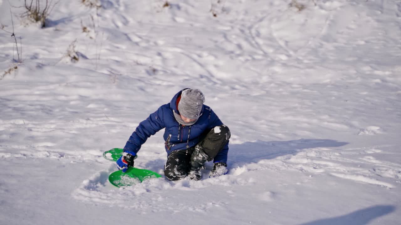 Child boy having fun, playing with plastic sledge while having snowy winter walk in nature. Frost winter season. Cute little boy with spade plays with snow on a winter day. Winter games and fun