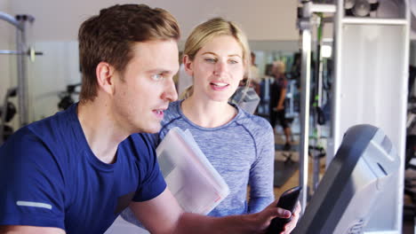 man exercising on cycling machine being encouraged by personal trainer in gym