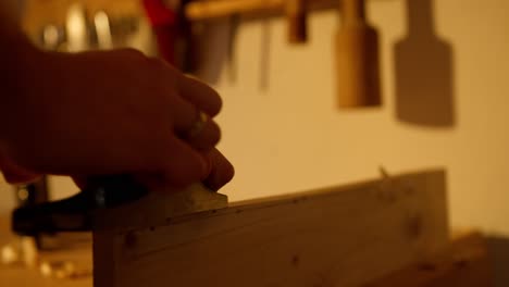 Boy-making-back-and-forth-motions-filing-the-edge-of-a-wooden-board-in-a-workshop