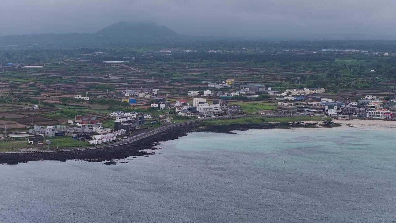 Toma horizontal en cameo avanzando con dolly hacia la derecha sobre la playa de Gimnyeong en la isla de Jeju, Corea del Sur, mostrando la costa, el pueblo, las tierras de cultivo, el océano y las rocas volcánicas