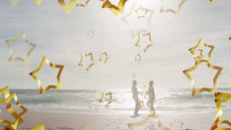 animation of gold christmas stars over happy silhouetted couple dancing on sunny beach