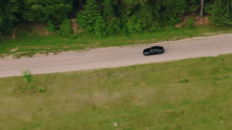 Car-driving-on-a-tarmac-road-near-green-forests-and-fields,-tracking-aerial-close-up-shot