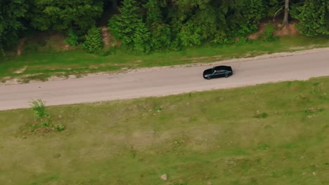 car driving on a tarmac road near green forests and fields, tracking aerial close up shot