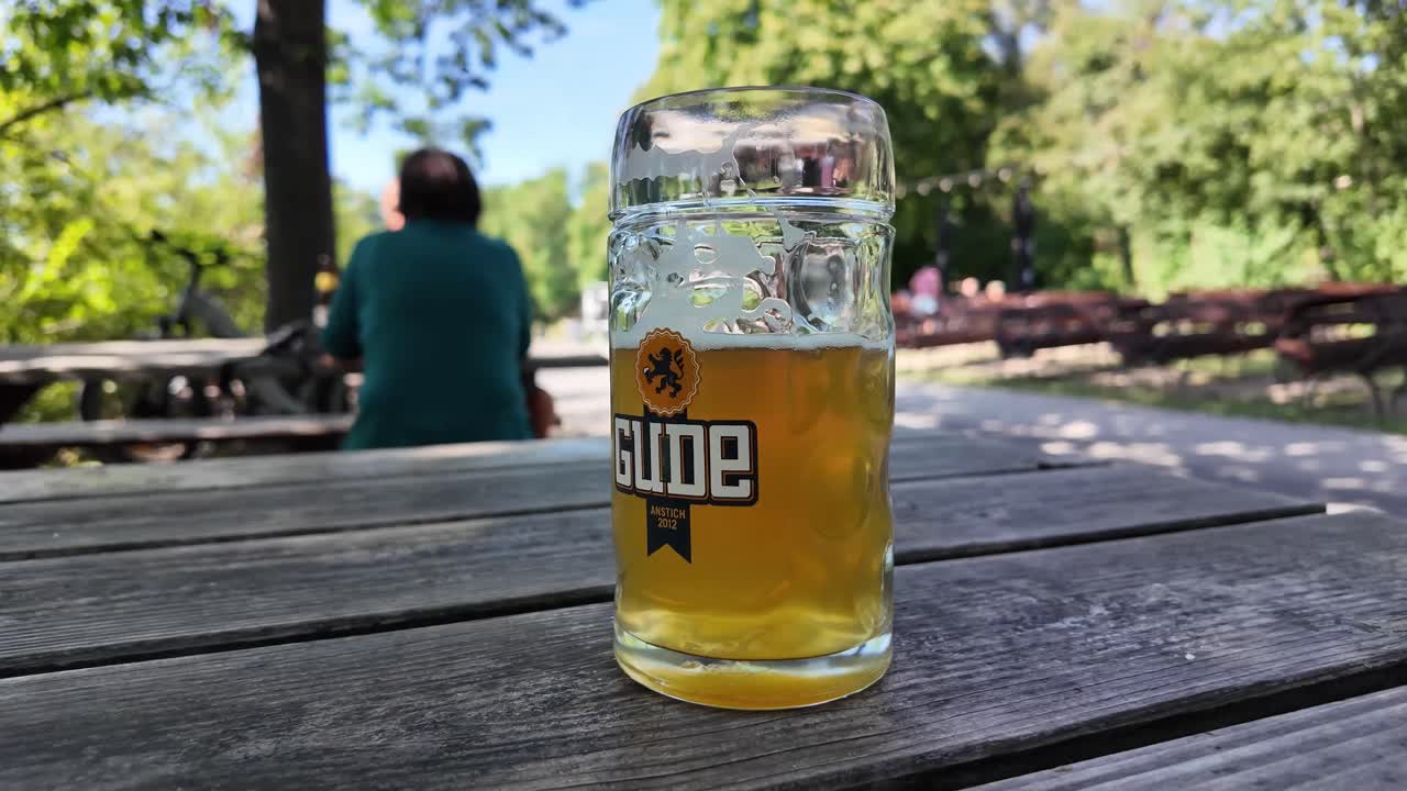 Sitting on the benches in a park with pint of beer on a wooden table, people around. Aschaffenburg castle promenade and shaded beer garden. Germany