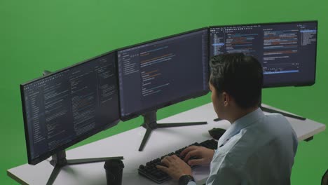vista lateral de un hombre asiático desarrollador pensando en algo luego levantando su dedo índice mientras escribe código con múltiples pantallas de computadora en el estudio de pantalla verde