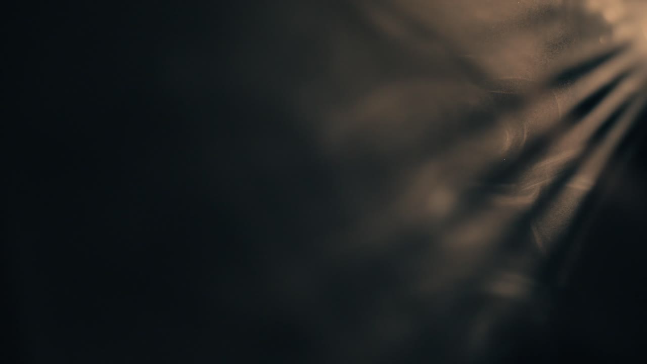 Des rayons de lumière dorés filtrent à travers une atmosphère sombre et texturée. La lumière chaude contraste avec l'obscurité environnante, mettant en évidence des particules de poussière dansant dans les rayons obliques.