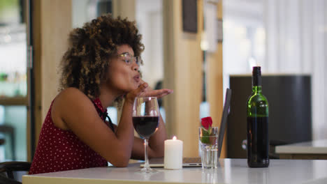 Mixed-race-woman-having-a-romantic-dinner-blowing-kisses-on-video-chat-at-home