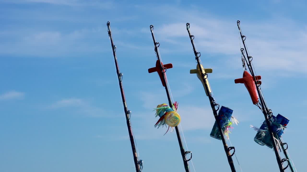 Fishing rods with colorful lures sway gently against a clear blue sky in Phuket, Thailand. Bright daylight enhances the vivid colors