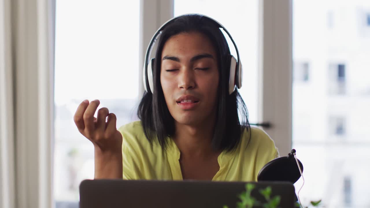 Mixed race gender fluid person recording a podcast using laptop at home