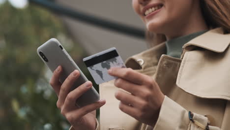 kaukasische studentin, die im freien mit dem smartphone online einkaufen.