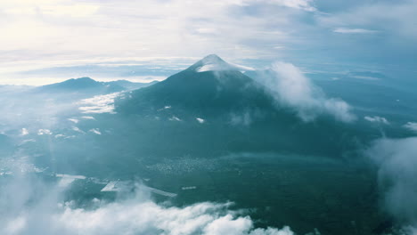 Plataforma-Aérea-Panorámica-Al-Volcán-Con-Una-Espesa-Capa-De-Nubes-Rompiéndose-Para-Revelar-El-Cono-Y-La-Ciudad