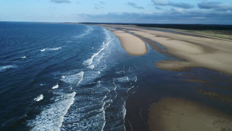 High-Aerial-Drone-Shot-Flying-Along-Big-Empty-Sandy-Beach-with-Bird-Flying-and-Small-Waves-Breaking-on-Sunny-and-Cloudy-Day-North-Norfolk-UK