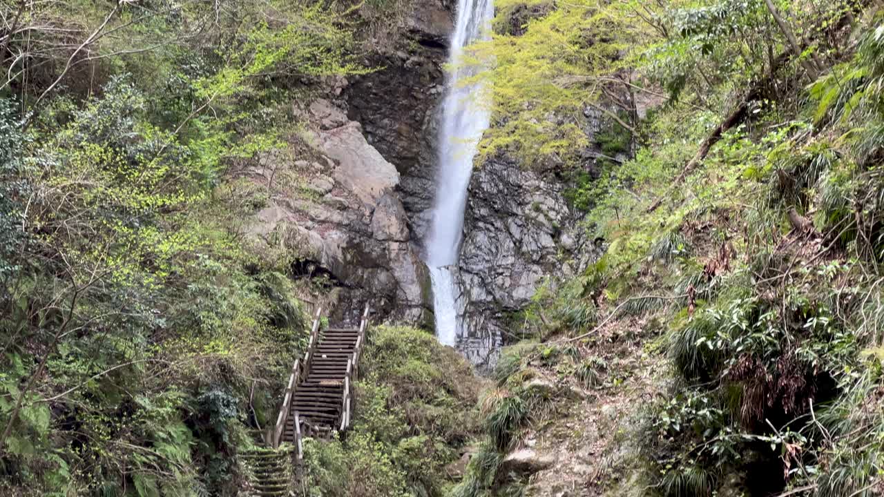 Slow motion tilt down over massive waterfall in Japanese nature