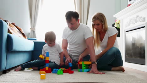 familia feliz padre madre y bebé 2 años jugando a lego en su luminosa sala de estar. rodaje a cámara lenta familia feliz