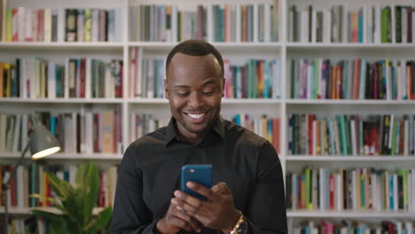 Retrato-De-Un-Joven-Afroamericano-Usando-Un-Teléfono-Inteligente-Riéndose-De-Pie-En-Las-Redes-Sociales-De-La-Biblioteca