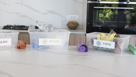 Three-labeled-bins-for-sorting-glass,-plastic,-and-paper-are-on-a-kitchen-counter-with-copy-space