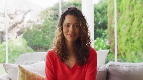 Portrait-of-biracial-woman-sitting-on-sofa,-looking-at-camera-and-smiling