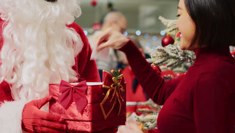 santa claus in festive adorn fashion shop holding collecting box acting as christmas present, receiving raffle ticket from asian client hoping to win big prize during winter holiday season