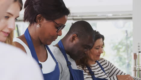 male and female adult students taking part in cookery class in kitchen