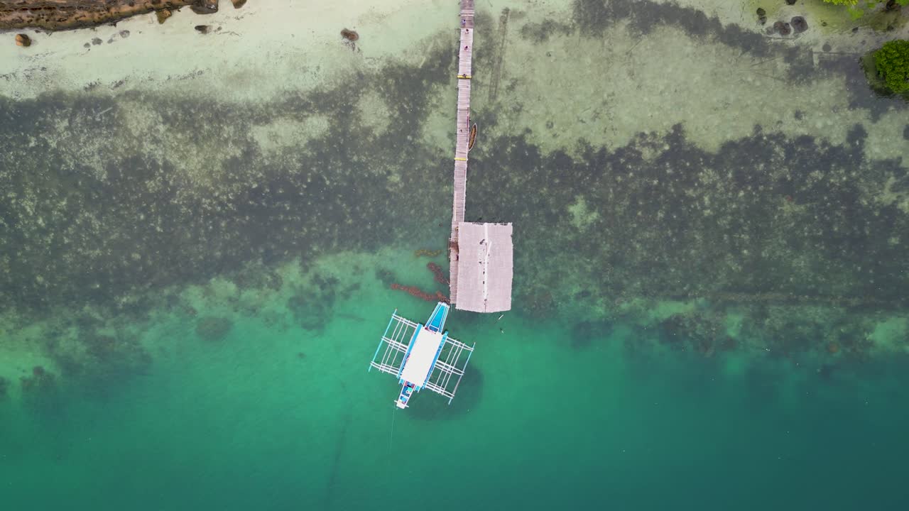Top down rising perspective of bangka outrigger canoe at wooden pier, aerial