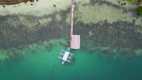 Top-down-rising-perspective-of-bangka-outrigger-canoe-at-wooden-pier,-aerial