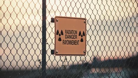 close-up of nuclear radiation danger sign on barbed wire perimeter fence with contaminated airborne radioactive particles in exclusion zone slow motion 4k