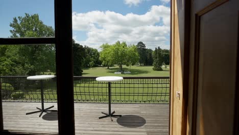 slowmotion shot from the inside to a balcony revealing a green park with big trees