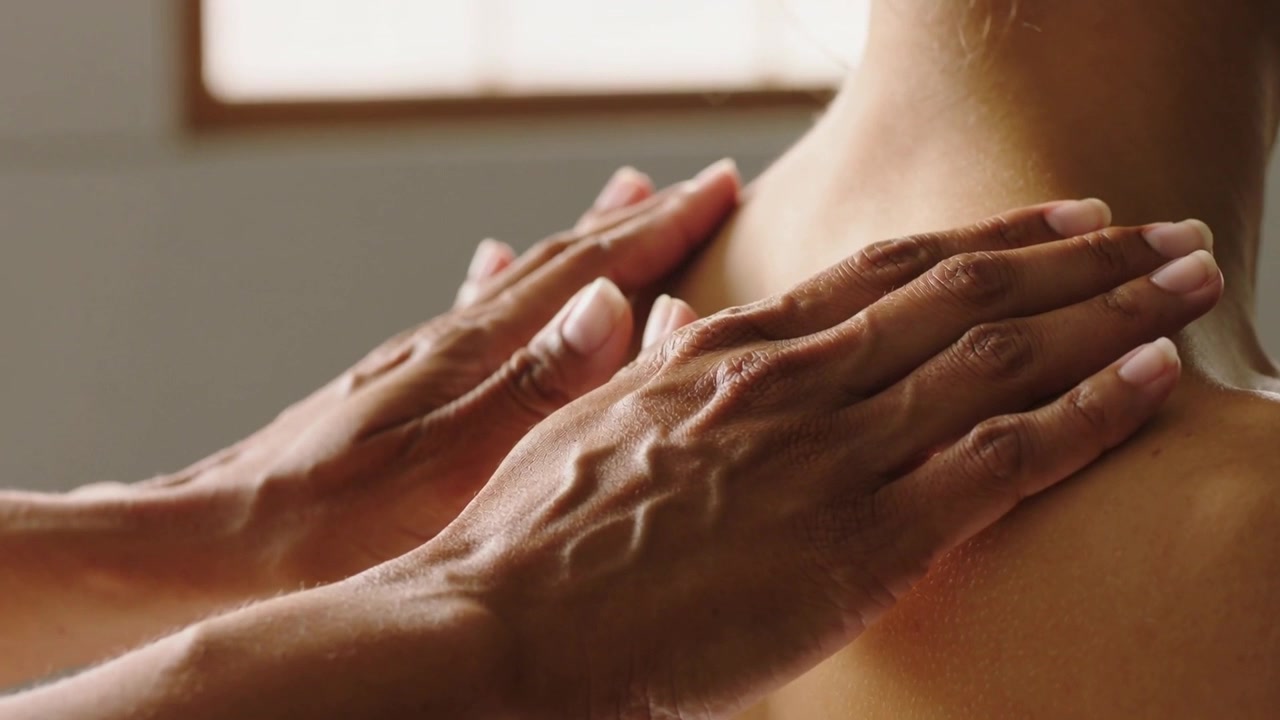 Les mains d'un thérapeute s'approchent, palpant et pressant le haut du dos et le cou exposés dans un spa.