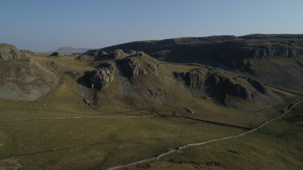 Ripresa aerea con drone a distanza che mostra il paesaggio campestre di Warrendale Knots, Yorkshire Dales, con erba e colline rocciose, pecore da fattoria e muretti a secco in una soleggiata giornata estiva nel Regno Unito.