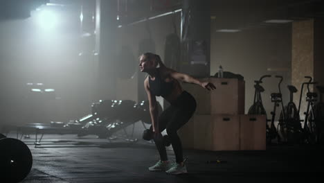 Una-Mujer-Fuerte-Hace-Esfuerzos-Y-Supera-Las-Dificultades-Levanta-Una-Pesa-En-Un-Gimnasio-Oscuro.-Mujer-Fitness-Levantando-Pesas-Entrenando-En-El-Gimnasio.