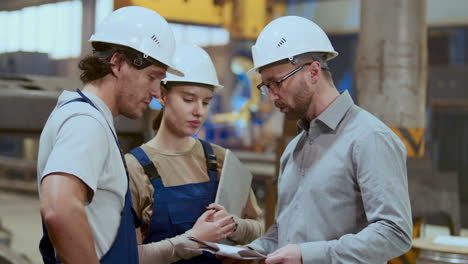 engineer and two workers discussing documents and tasks in industrial plant