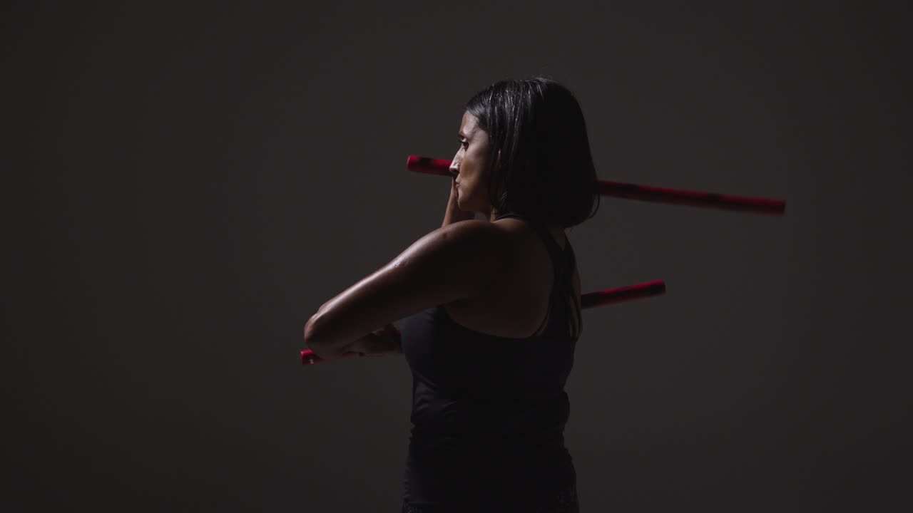 체육관 피트니스 옷을 입은 성숙한 여성이 무술 에스크리마 스틱으로 운동하는 스튜디오