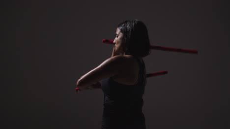 Foto-De-Estudio-De-Una-Mujer-Madura-Vistiendo-Ropa-De-Gimnasio-Haciendo-Ejercicio-Con-Palos-De-Escrima-De-Artes-Marciales