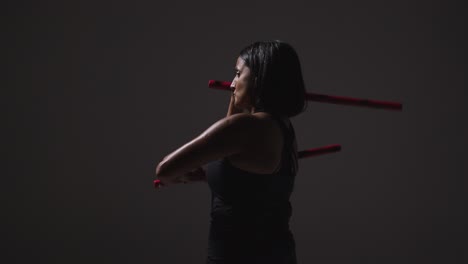 fotografía de estudio de una mujer madura con ropa de gimnasia haciendo ejercicio con palos de artes marciales