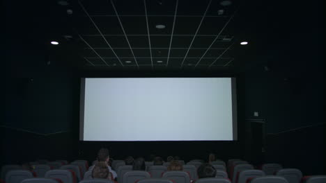 audience in cinema hall looking at white screen in anticipation of movie show