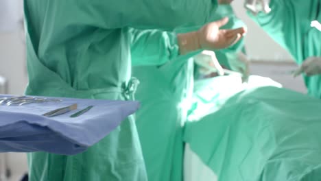 diverse surgeons wearing surgical gowns operating on patient in operating theatre, slow motion