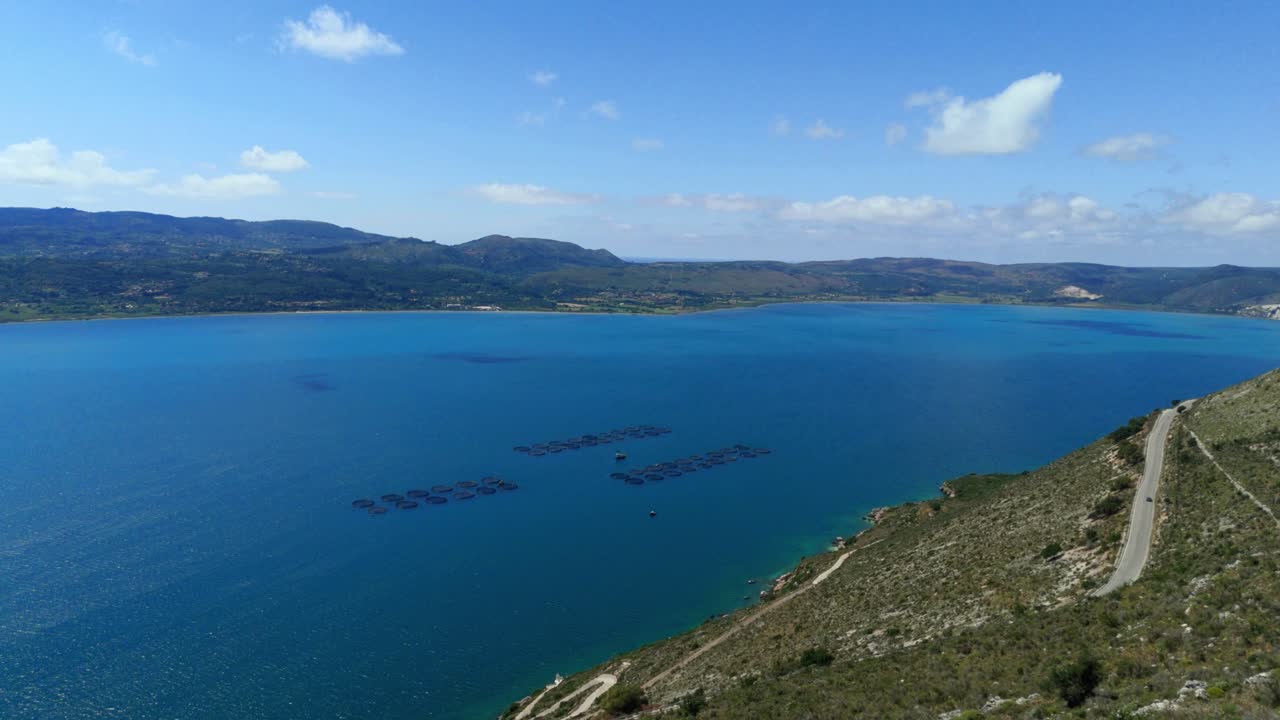 Aerial drone view of fish farms and sea pens in the clear blue waters of the Ionian Sea near Kefalonia, Greece. Aquaculture structures surrounded by natural seascape on a sunny day.