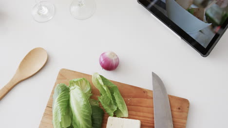 vegetables, cheese, knife, chopping board and tablet on kitchen worktop, copy space, slow motion