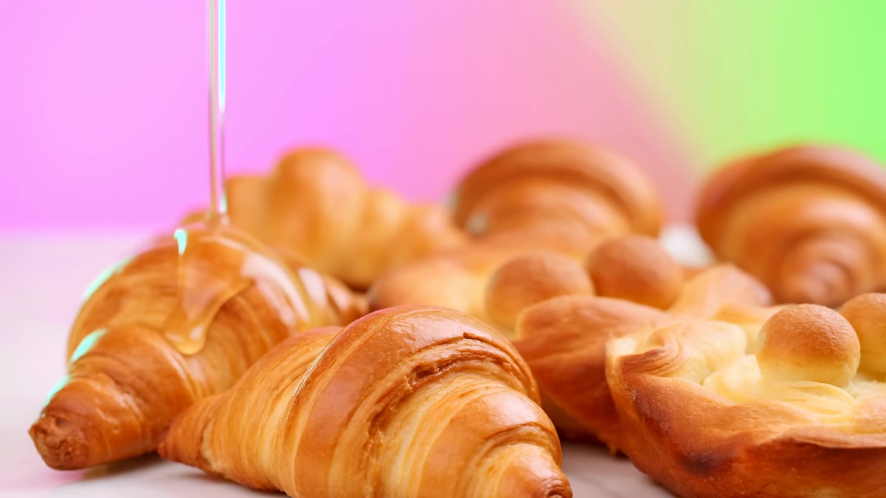 Croissant dorati con filo di miele, primo piano, sfondo pastello. Scena di panetteria artigianale che mostra una pasta sfoglia burrosa e friabile