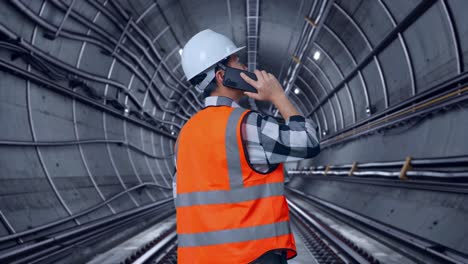 back view of asian male engineer with safety helmet talking on smartphone while standing in underground subway tunnel