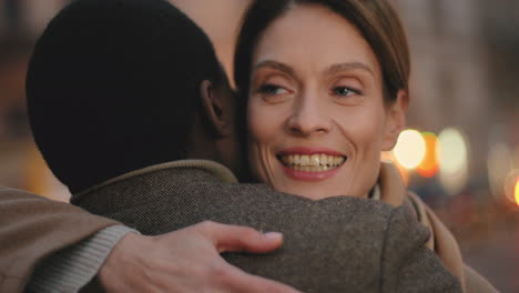 rear view of young african american man hugging a caucasian smiling woman in the street in the evening