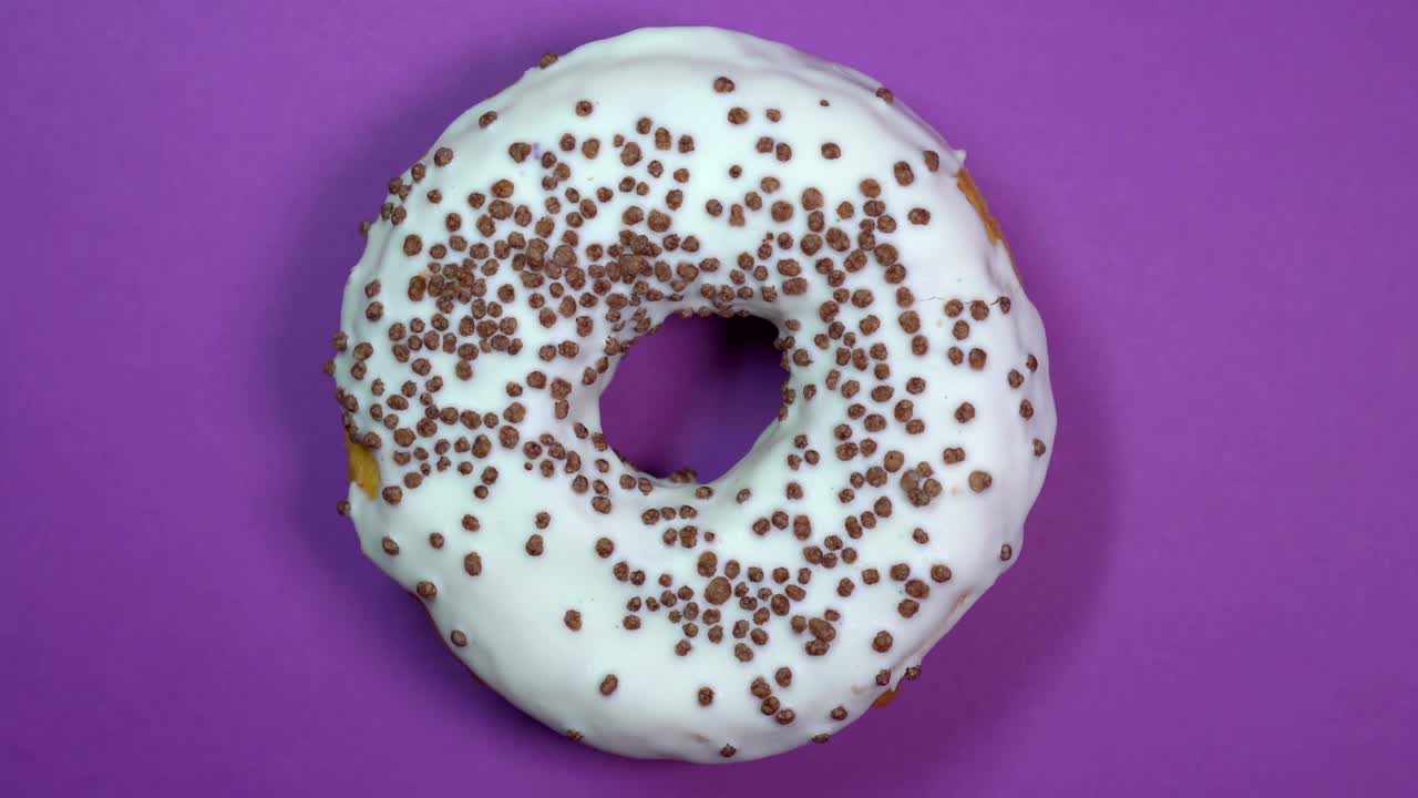 donut brillante y blanco con bolas de chocolate, macro disparado, girando sobre un fondo púrpura.
