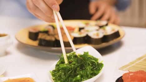 vista ravvicinata delle mani dell'uomo giapponese che tengono le bacchette raccogliendo alghe wakame in cucina