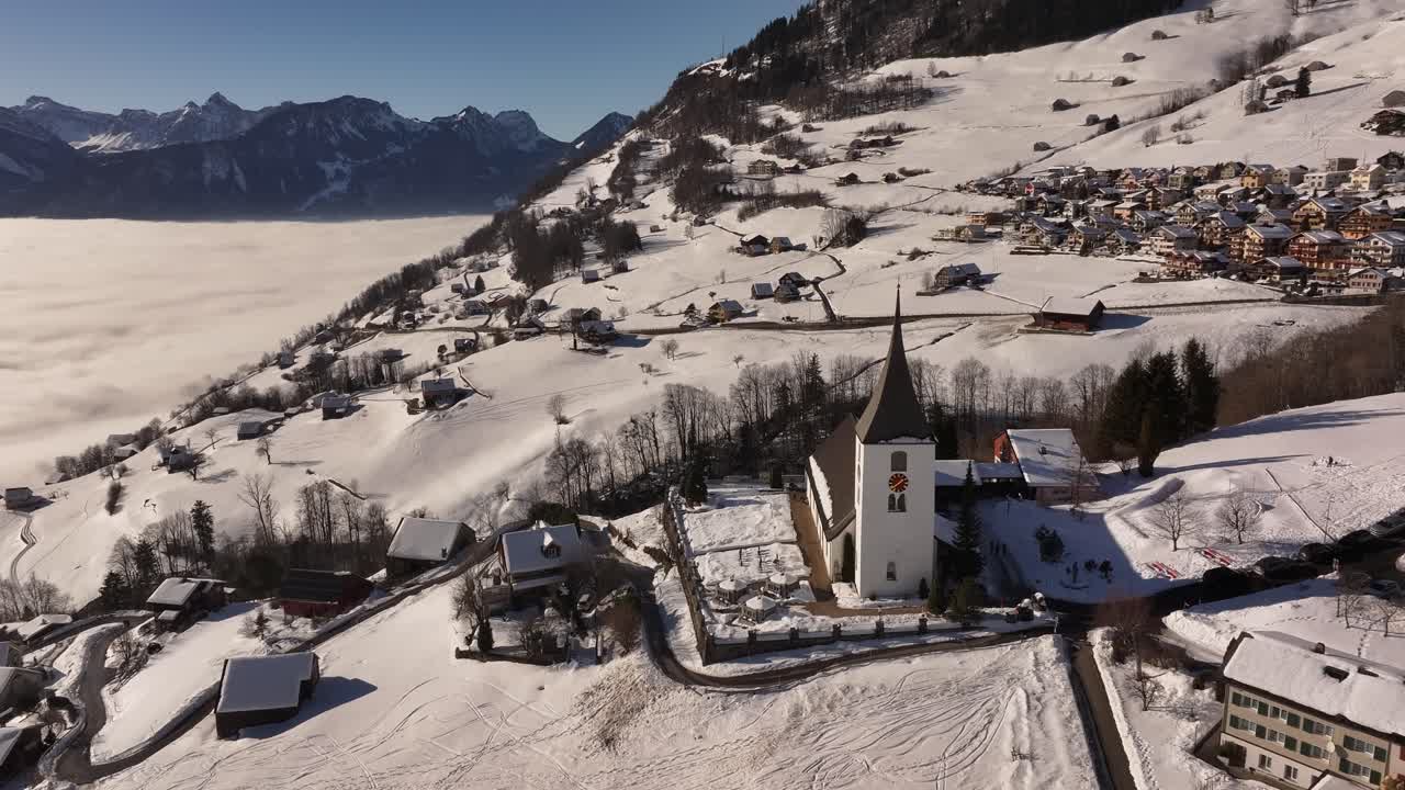 Snow-covered church and alpine village on a hillside overlooking foggy Walensee in Amden Switzerland