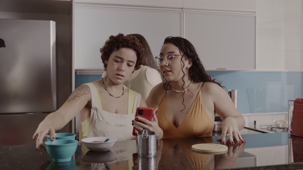 Mujeres en una cocina usando un smartphone mientras preparan comida